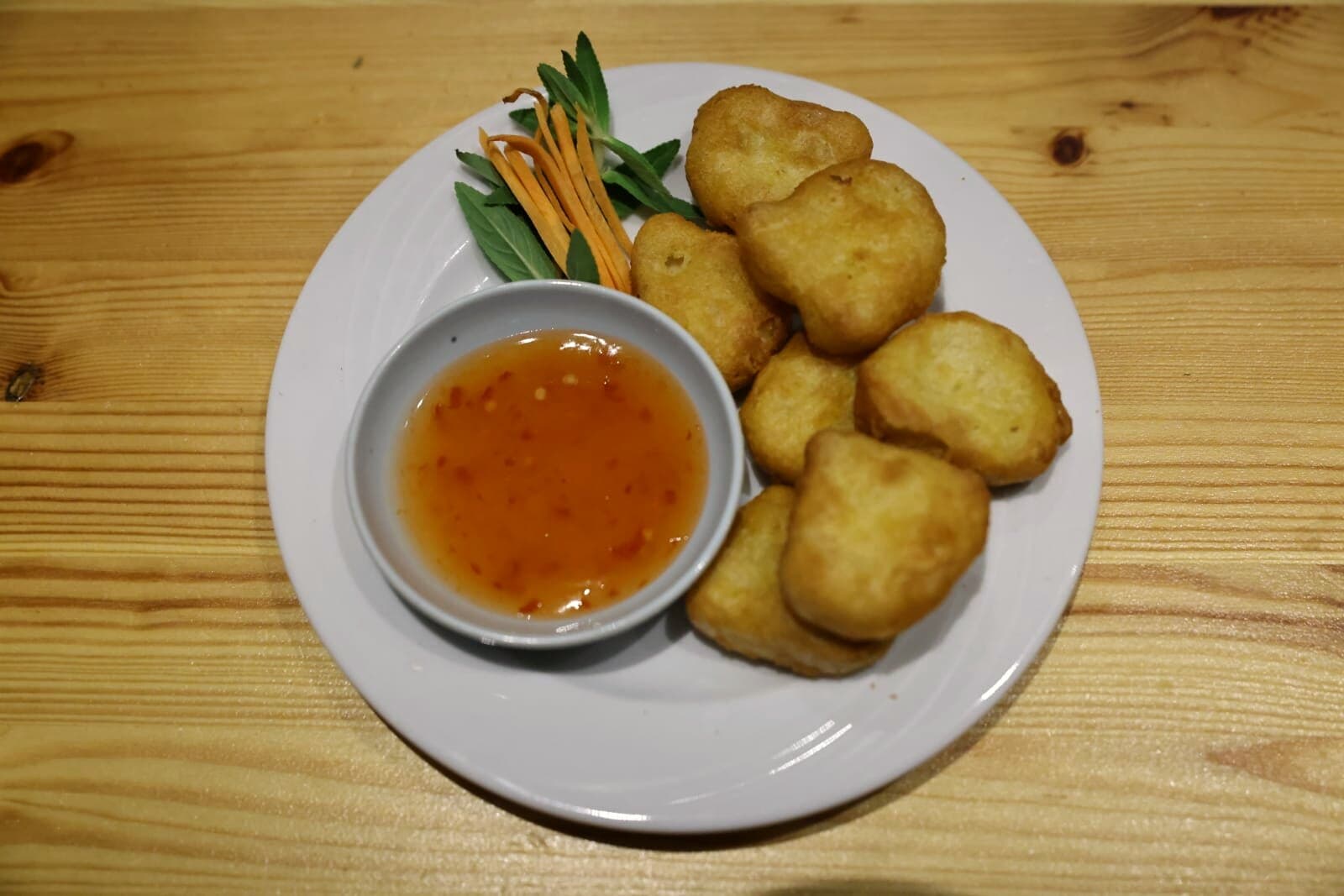Frittierte Stücke im Teigmantel auf einem weißen Teller, daneben ein Schälchen rötliche Sauce und Karottenstreifen