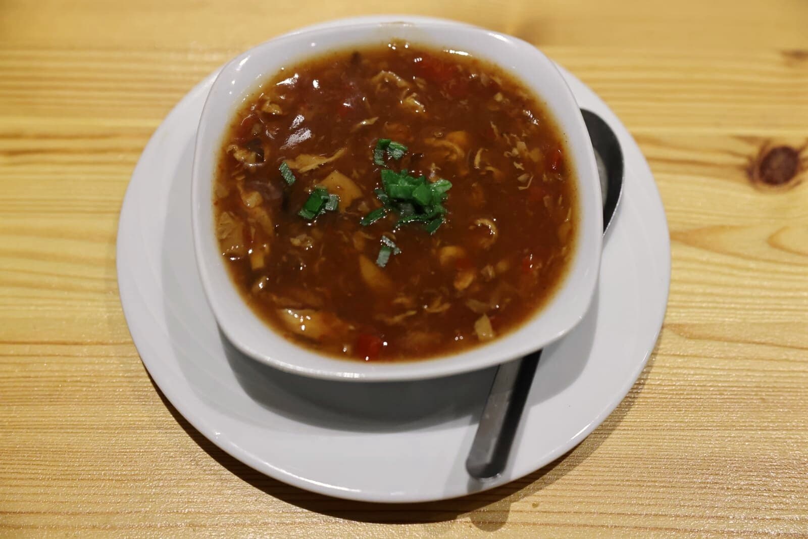 Scharf-Sauer-Suppe in einer weißen Schale auf einem Holztisch