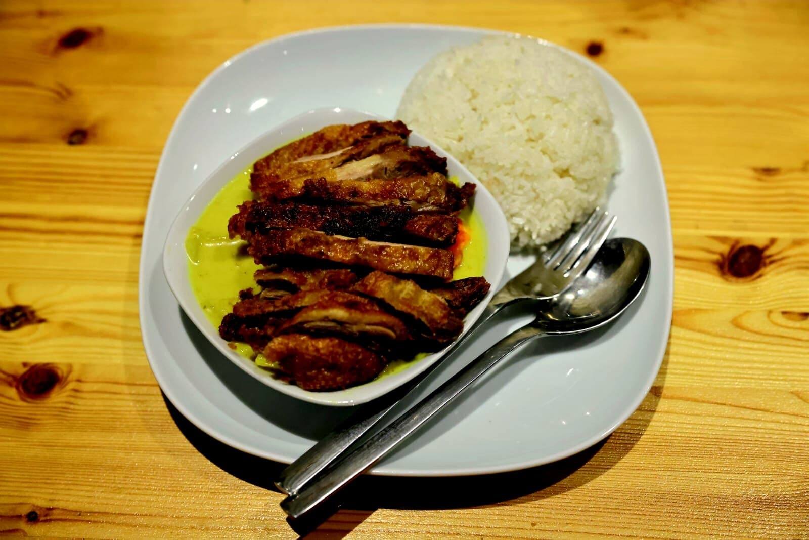Knuspriges Hähnchen auf Curry-Sauce, daneben Reis, auf einem weißen Teller